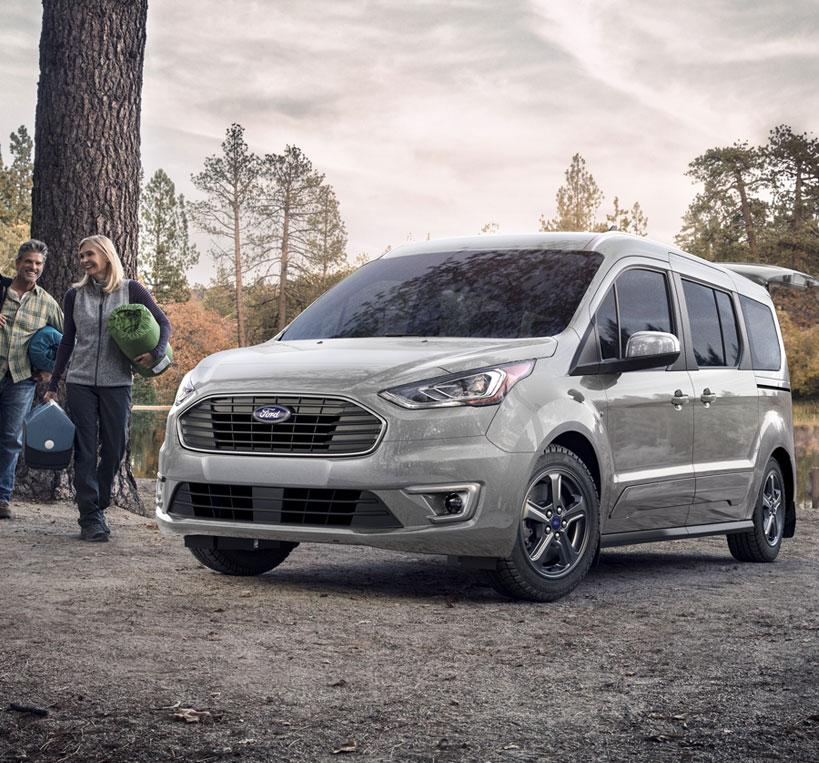 Couple about to pack up their 2022 Ford Transit Connect Cargo Van with sleeping bags on their camping trip in the woods