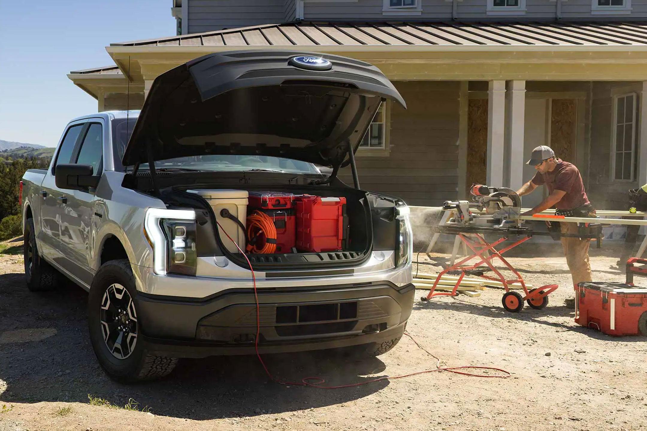 Man using a power saw in front of his house that is plugged into a 2022 Ford F-150 Lightning | South Bay Ford