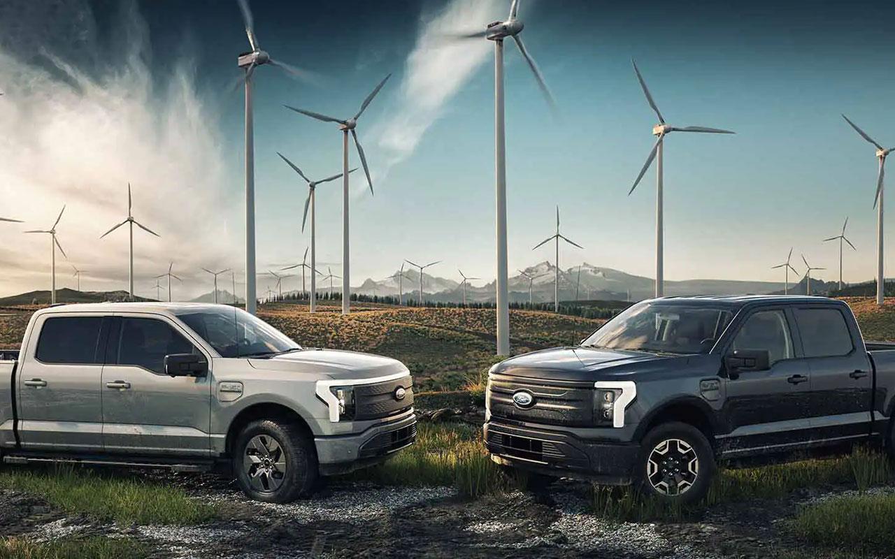 Two 2022 Ford F-150 Lightning trucks parked in a field with windmills