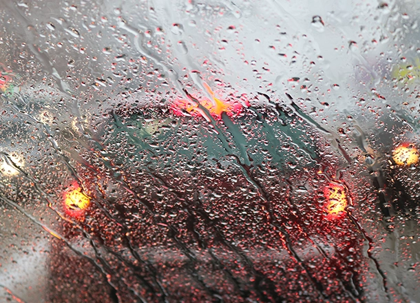 Gathered rain on blurry windshield obscuring view of car with brake lights